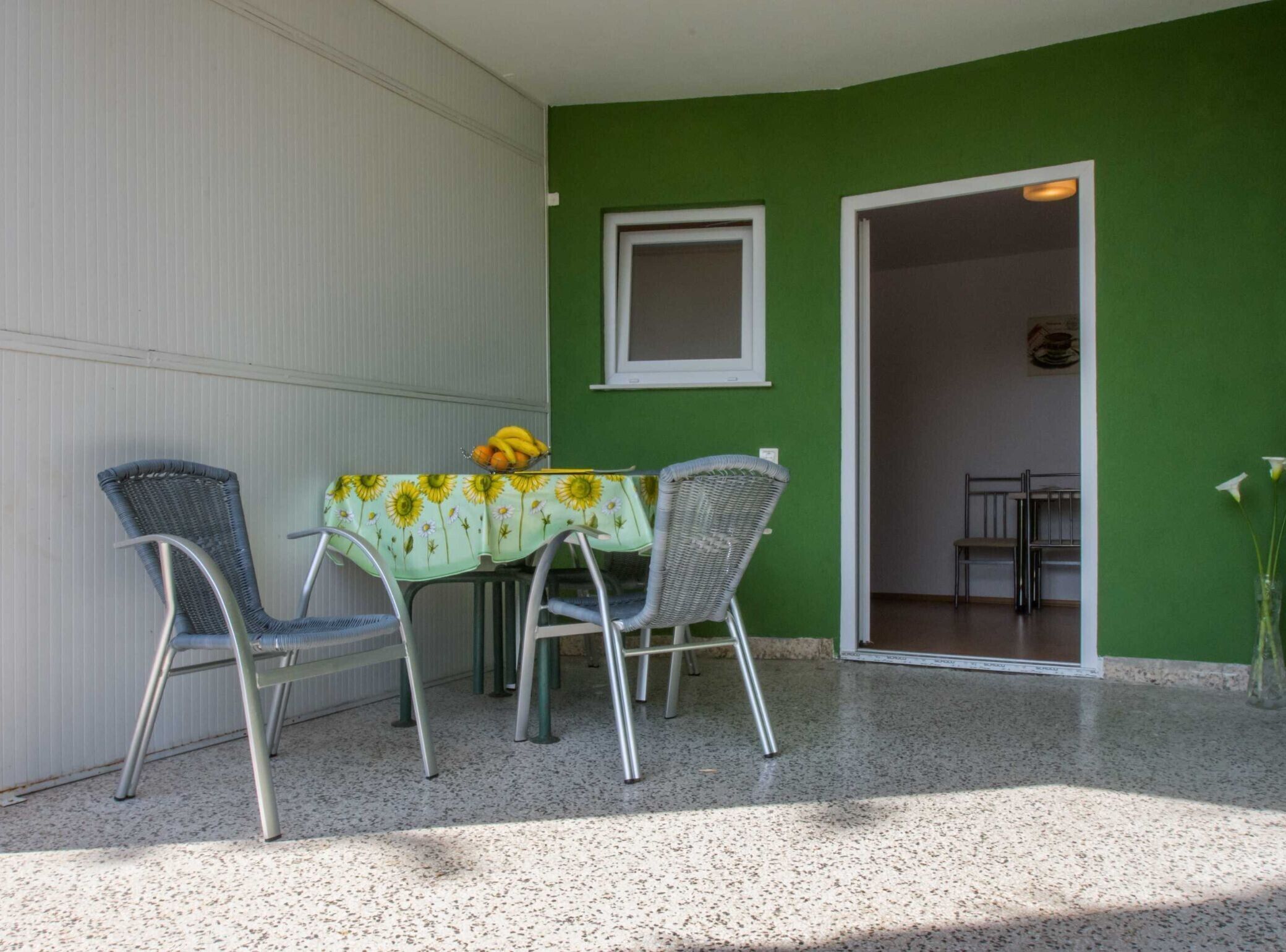 A patio with a table and two chairs, a small window, and a door leading to an interior space.