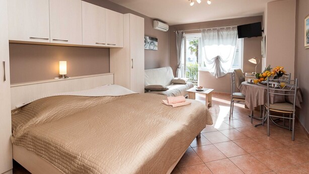 A hotel room with a large bed, a desk with a chair, a small table with a lamp, and a TV mounted on the wall. - Beachfront Crikvenica Apartments with Sea View - Standard Studio Apartment with Sea View (Crikvenica)