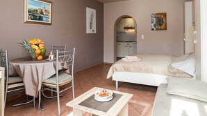 A compact hotel room with a bed, a small dining table with chairs, a kitchenette, and artwork on the walls. - Beachfront Crikvenica Apartments with Sea View - Standard Studio Apartment with Sea View (Crikvenica)