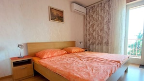 Une chambre à coucher avec un lit en bois, deux tables de chevet, une commode, un climatiseur fixé au mur, une fenêtre avec des rideaux et un tableau accroché au mur.