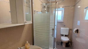 Une salle de bain dotée d’une douche à parois de verre, d’un lavabo avec distributeur de savon, de toilettes et d’une fenêtre laissant entrer la lumière naturelle.
