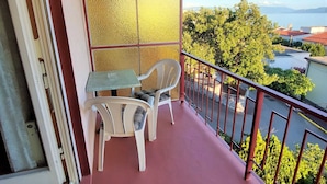 Un balcon avec une table et deux chaises, une vue sur un lac et une rambarde rouge.