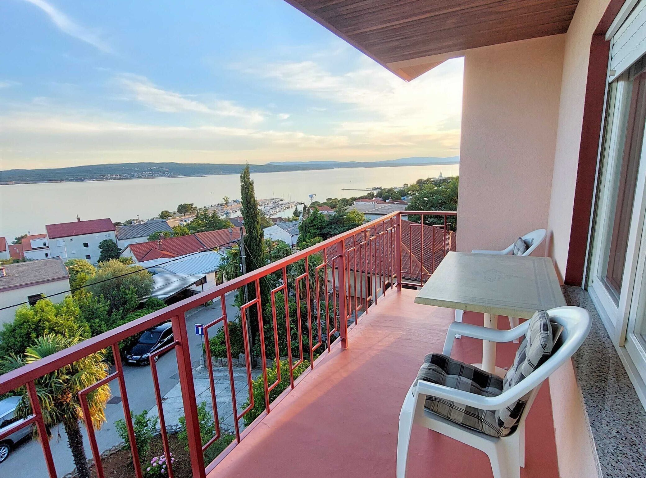 Ein Balkon mit Tisch und Stuhl, mit Blick auf ein Gewässer und Gebäude.