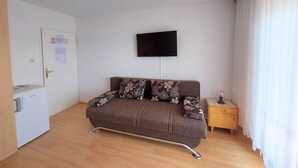 Une petite pièce meublée, comprenant un canapé, un téléviseur fixé au mur, une table d’appoint en bois et une porte avec une poignée.