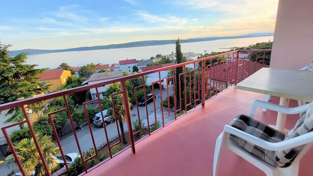 Un balcon donnant sur une étendue d’eau, avec une rambarde rouge et une chaise blanche.