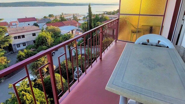 A balcony with a table and chairs, overlooking a residential area and a body of water.