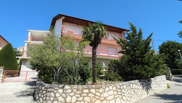 Un immeuble à plusieurs étages doté de balcons, entouré de murs de pierre et de verdure.