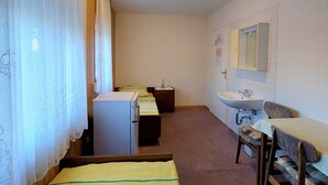 Une petite pièce, de taille modeste, comprenant un lit, un bureau, une chaise, un lavabo et un miroir.