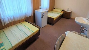 Une petite chambre, de taille modeste, comprenant deux lits simples, un petit réfrigérateur, une table de chevet et un lavabo.