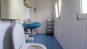 Un bagno con un water bianco, un lavandino blu e un mobiletto a scaffali in metallo.