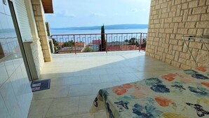 Un balcone con pavimento piastrellato, un letto con copripiumino floreale e vista su un corpo d'acqua e colline lontane.
