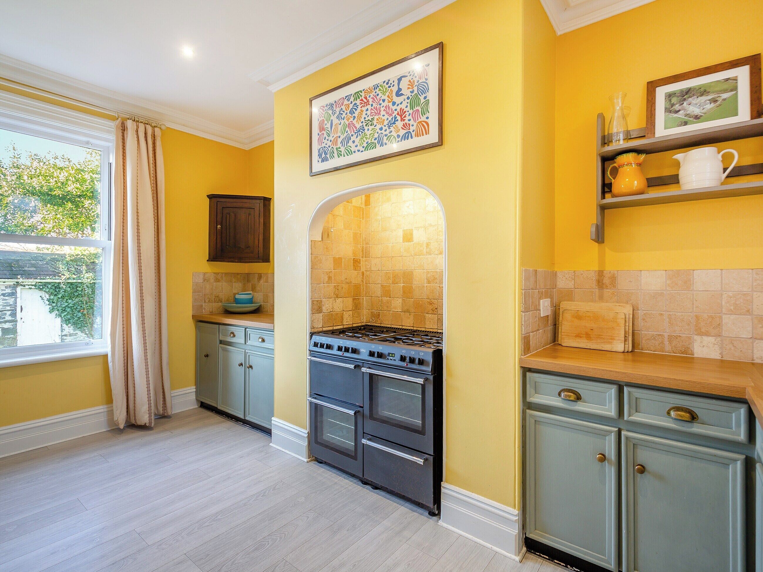 Una cocina con estufa, armarios y una ventana con cortinas.