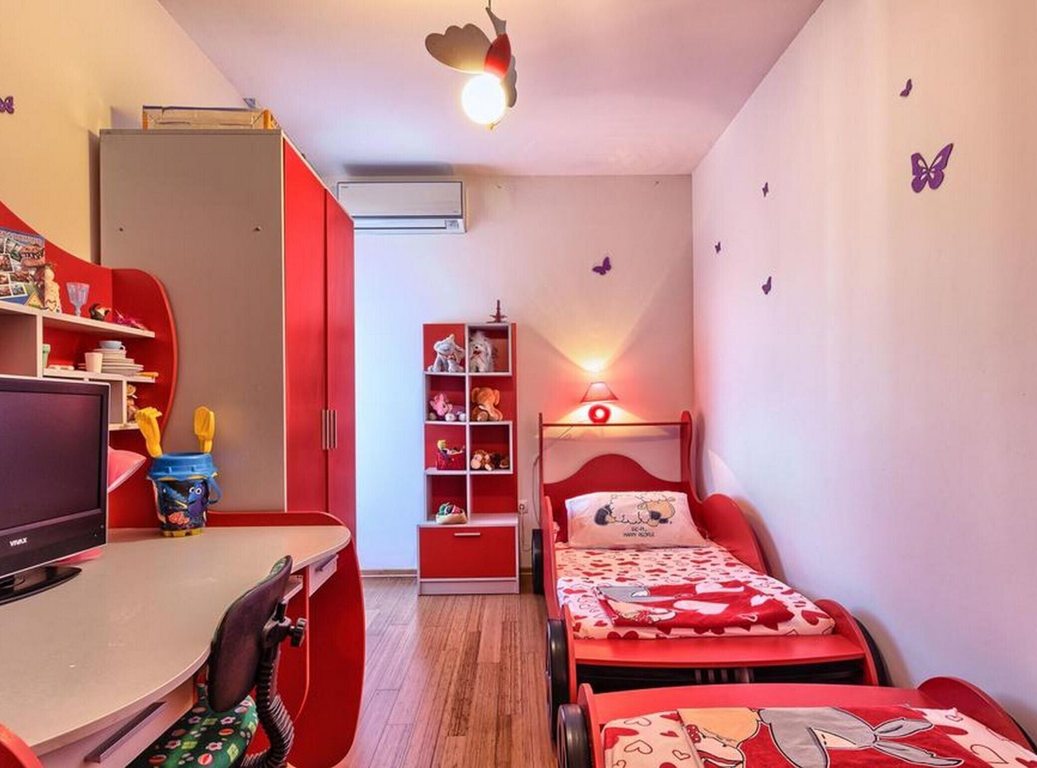 A compact bedroom with a desk, a bed, a wardrobe, and a shelf with toys.