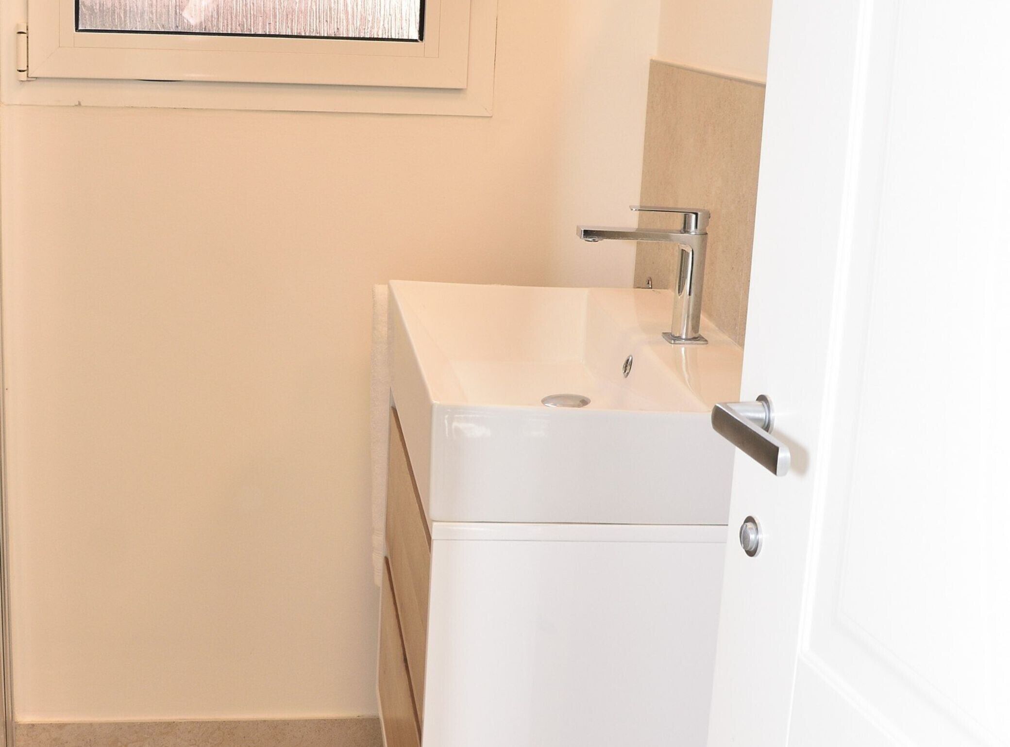 Un bagno piccolo e bianco con un lavandino, uno specchio e una porta.