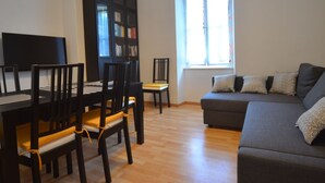 Una sala de estar con una mesa de comedor, sillas, un sofá, una estantería y una ventana con cortinas.