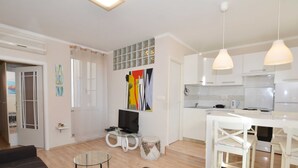 Un appartement moderne comprenant un salon, un coin repas et une cuisine. On y trouve un téléviseur posé sur une table en verre, un canapé et une table à manger avec des chaises.