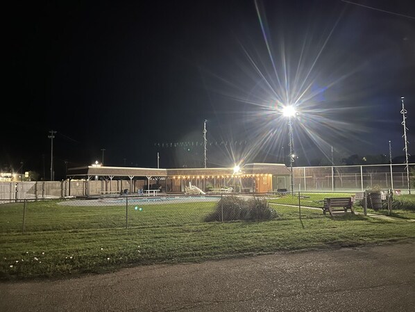 A well-lit sports facility at night with a fenced area, a covered seating area, and a small building with lights. - The Lodge (Bridgeport)