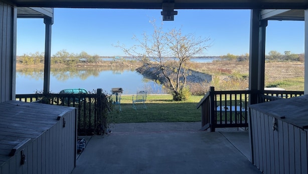 Eine überdachte Veranda mit Blick auf einen See und eine Wiese.