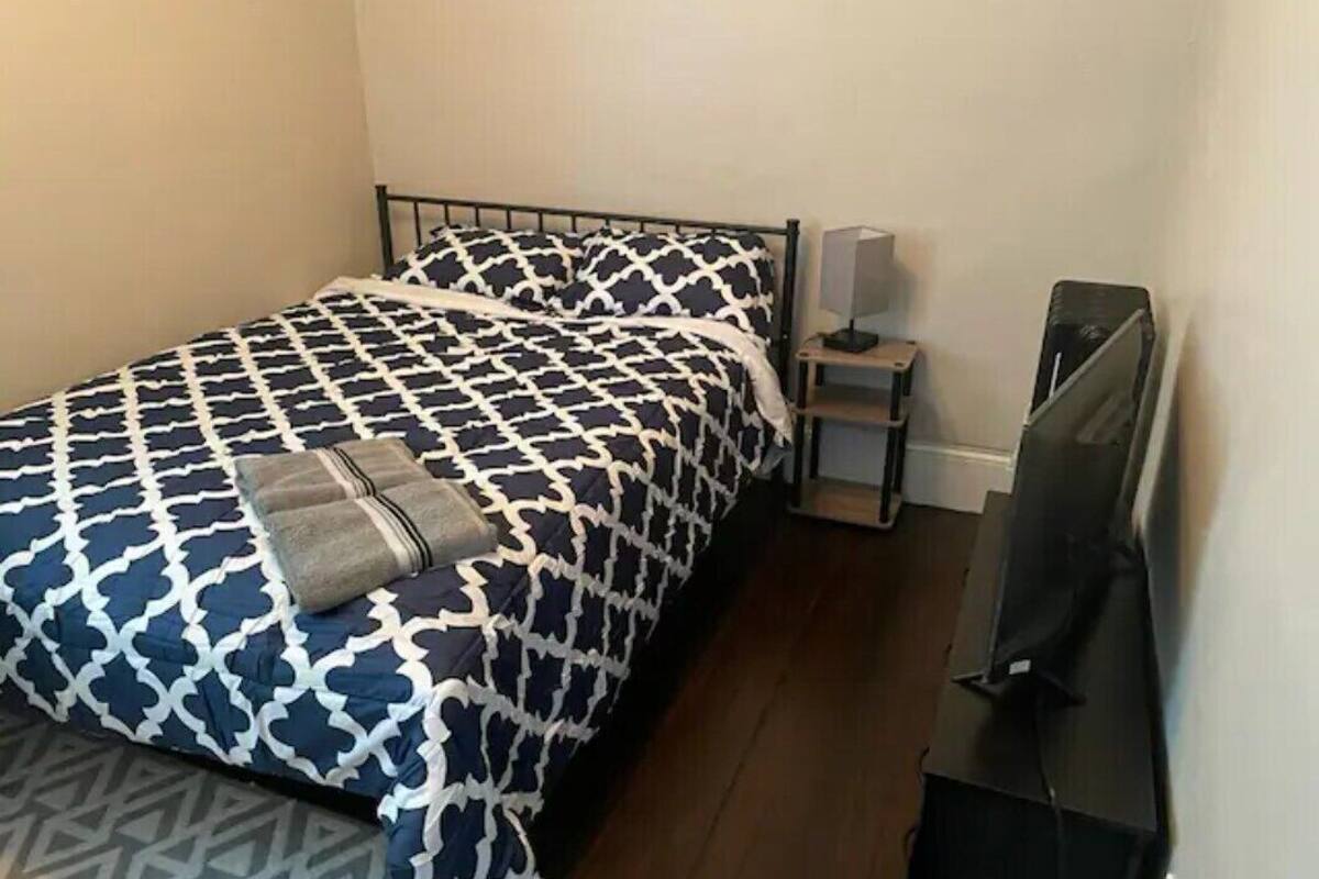 A single bed with a patterned bedspread, a bedside table with a lamp, and a television on a stand.