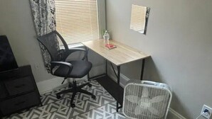 A small office space with a desk, chair, and a standing fan. - Homestay In Fields Corner Area Boston (Boston)