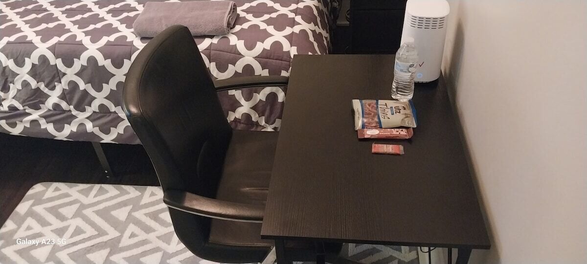 Una habitación pequeña con una cama, una silla, una mesa y una botella de agua.
