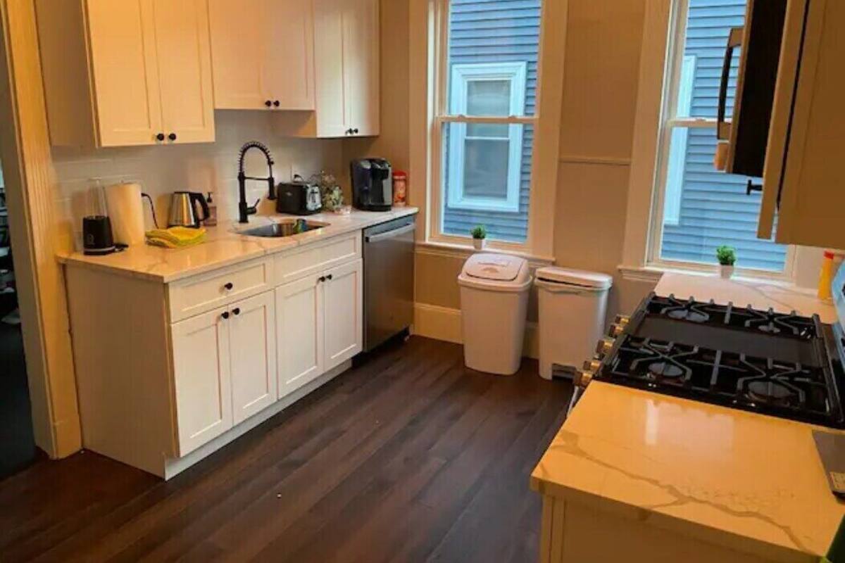 A kitchen with white cabinets, a stove, a sink, and a window with blinds.