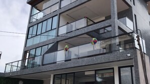 A modern building with multiple balconies, large windows, and potted plants in front. - Apartamento Porto de Galinhas, Centro, Vista Mar, Ipojuca (Maracaipe Ipojuca)