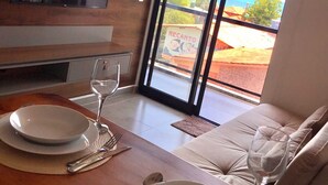 A dining area with a wooden table set for two, a television mounted on the wall, and a view of the ocean through large sliding doors. - Apartamento Porto de Galinhas, Centro, Vista Mar, Ipojuca (Maracaipe Ipojuca)