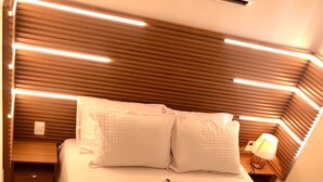 A neatly made bed with a white quilt and two pillows, a bedside lamp, and a wall-mounted air conditioner. - Apartamento Porto de Galinhas, Centro, Vista Mar, Ipojuca (Maracaipe Ipojuca)