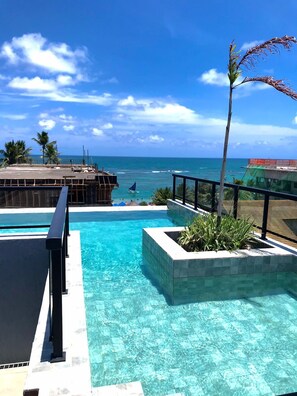 A clear blue pool with a view of the ocean and palm trees. - Apartamento Porto de Galinhas, Centro, Vista Mar, Ipojuca (Maracaipe Ipojuca)