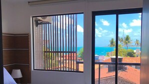 A bedroom with a large bed, a window with a view of the ocean, and a balcony with a railing. - Apartamento Porto de Galinhas, Centro, Vista Mar, Ipojuca (Maracaipe Ipojuca)