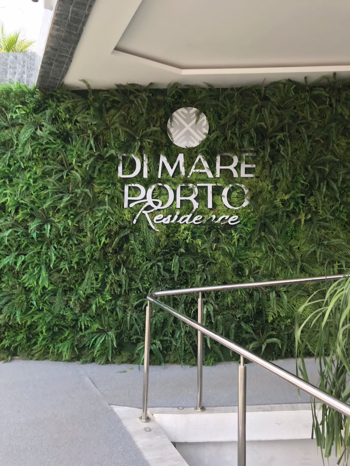 A sign with the text "DI MARE PORTO Residence" against a backdrop of green foliage.