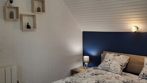 A bedroom with a bed, a hanging light fixture, and three wall-mounted shelves with decorative items. - Gite de Pennenez  (Plomodiern)