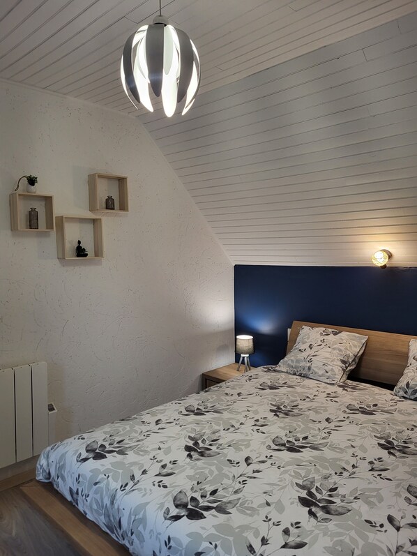 A bedroom with a bed, a hanging light fixture, and three wall-mounted shelves with decorative items.