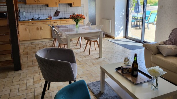 A modern kitchen with wooden cabinets and a tiled backsplash, a dining area with a white table and chairs, and a living area with a sofa and a coffee table. - Gite de Pennenez  (Plomodiern)