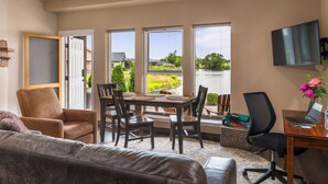 A living room with a couch, a dining table with chairs, a TV mounted on the wall, and a view of a lake. - Modern one bedroom in quiet lakeside retreat near wineries, dock, boats and more! (Zillah)