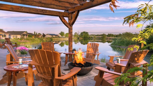 A patio with wooden chairs and tables, a fire pit, and a view of a lake and houses in the background. - Modern one bedroom in quiet lakeside retreat near wineries, dock, boats and more! (Zillah)