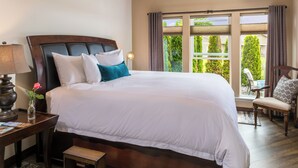 A large bed with white bedding, a bedside table with a lamp, a small table with a vase of flowers, and a chair with a cushion. - Modern one bedroom in quiet lakeside retreat near wineries, dock, boats and more! (Zillah)