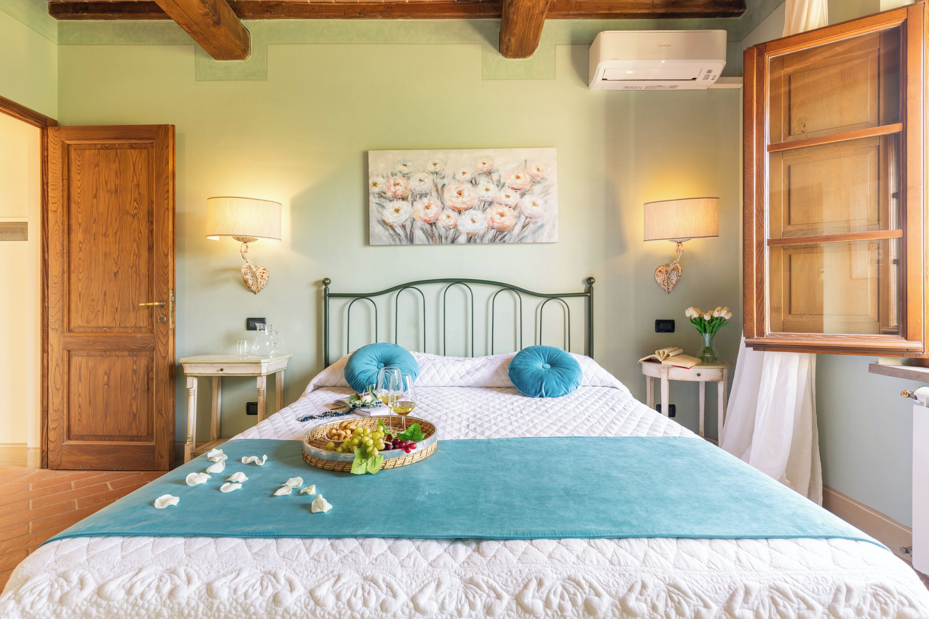 A neatly arranged bedroom with a bed, two bedside tables, a wall-mounted lamp, and a painting.
