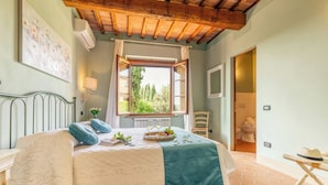Un dormitorio con cama, ventana, una silla y una mesita.