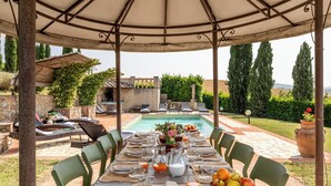 Comedor con mesa dispuesta para seis personas, piscina exterior y vistas al jardín.