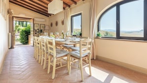 Un comedor con una mesa y sillas de madera, un ventanal con vistas al campo, y piso de baldosas.