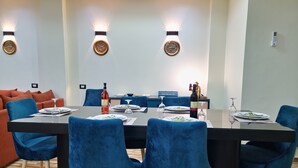 Un comedor con una mesa dispuesta para cuatro personas, sillas azules y una botella de vino.
