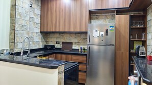 Cocina moderna con protector contra salpicaduras de piedra, armarios de madera, refrigerador de acero inoxidable y encimera negra.
