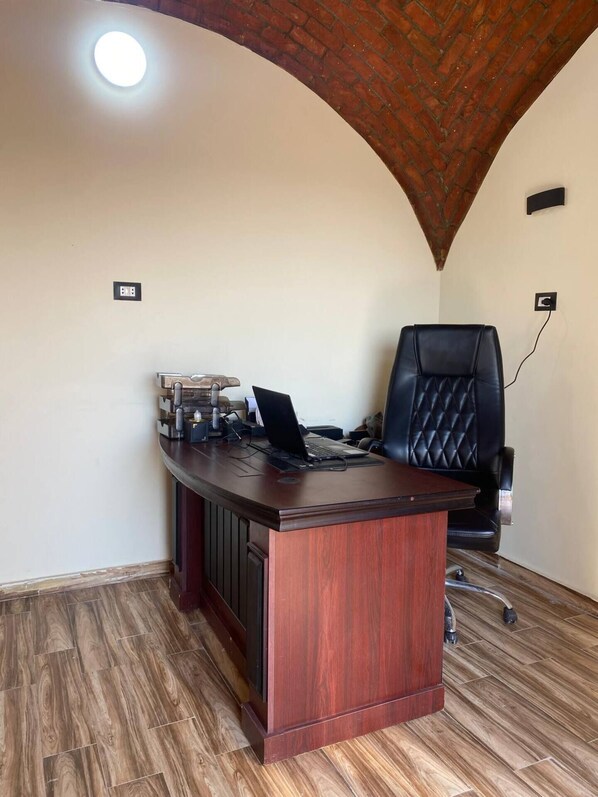 A wooden desk with a laptop, a black leather chair, and a ceiling light.