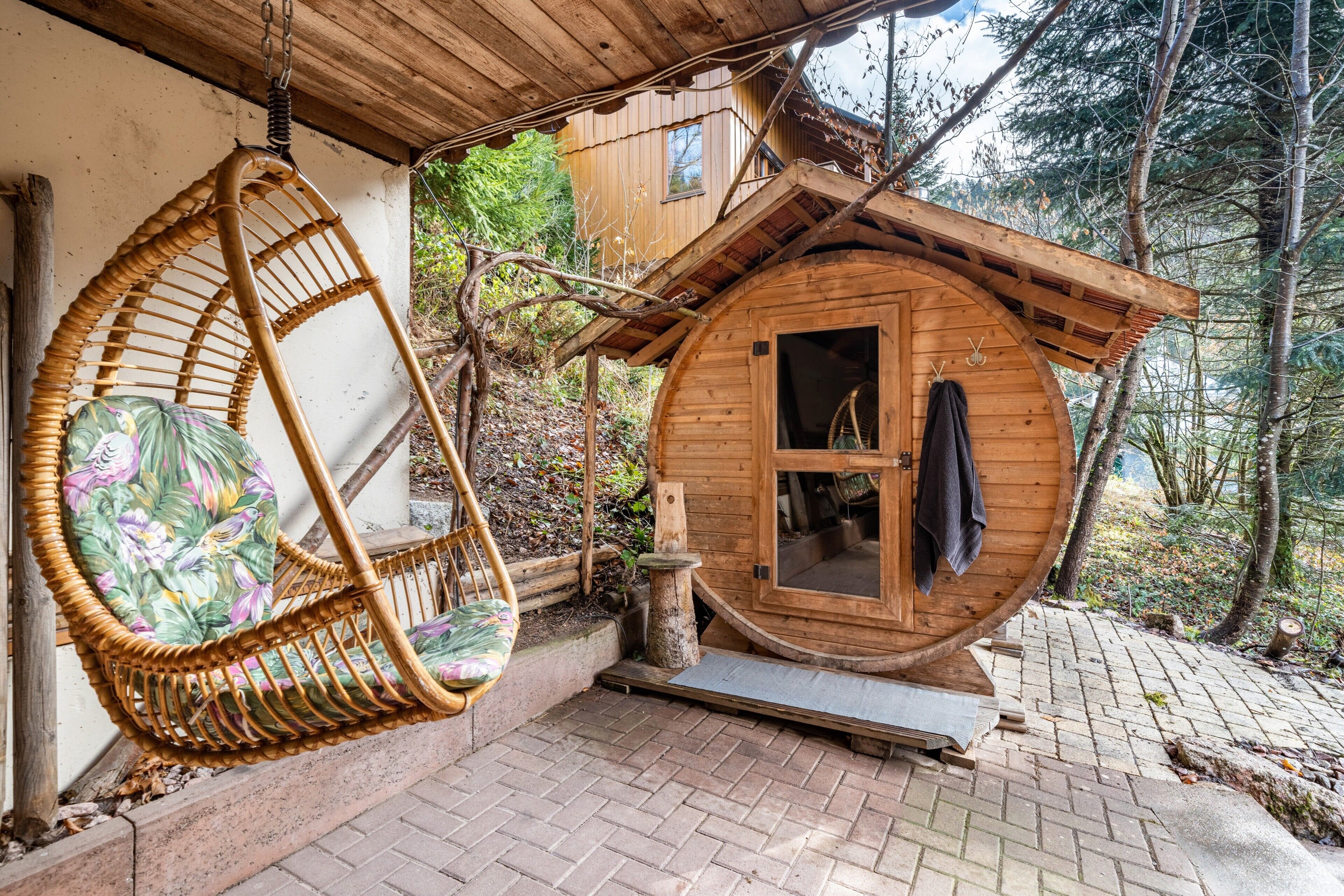 Une cabane en bois avec une porte ronde, une chaise suspendue et un chemin pavé de briques.