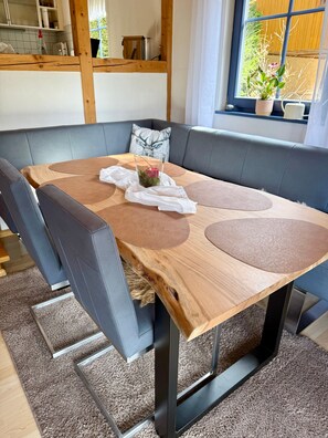 A dining table with a unique wooden top, surrounded by cushioned chairs, in a room with a view of a garden through a window. - Holiday Home 'Elisabeth' with Barrel Sauna and Private Garden (Hornberg)