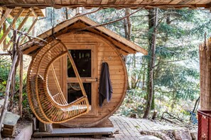 Une cabane en bois à la structure circulaire, avec une chaise suspendue et une porte sur laquelle est accrochée une serviette.