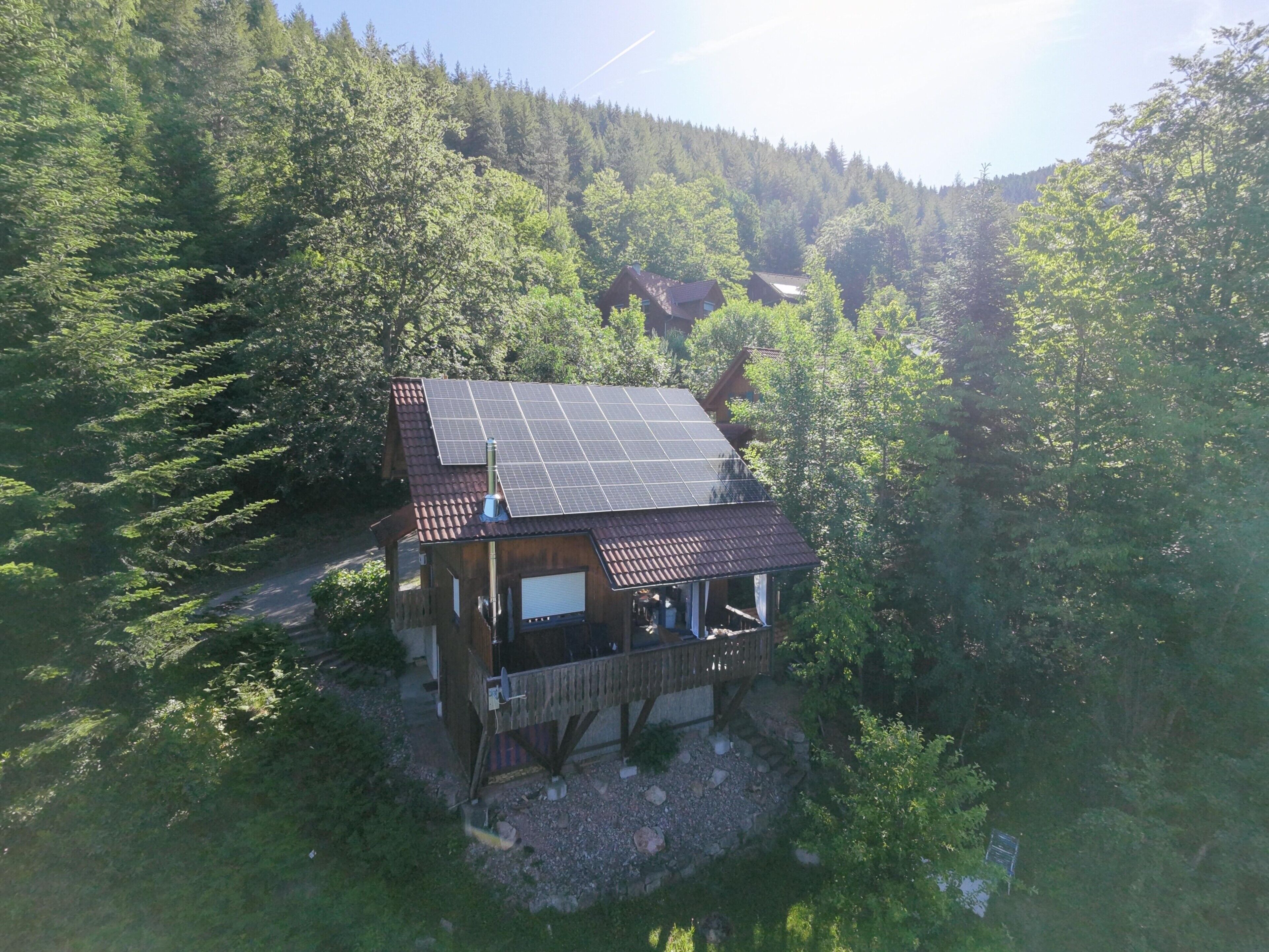 Eine Hütte mit Solardach, umgeben von dichtem Wald.