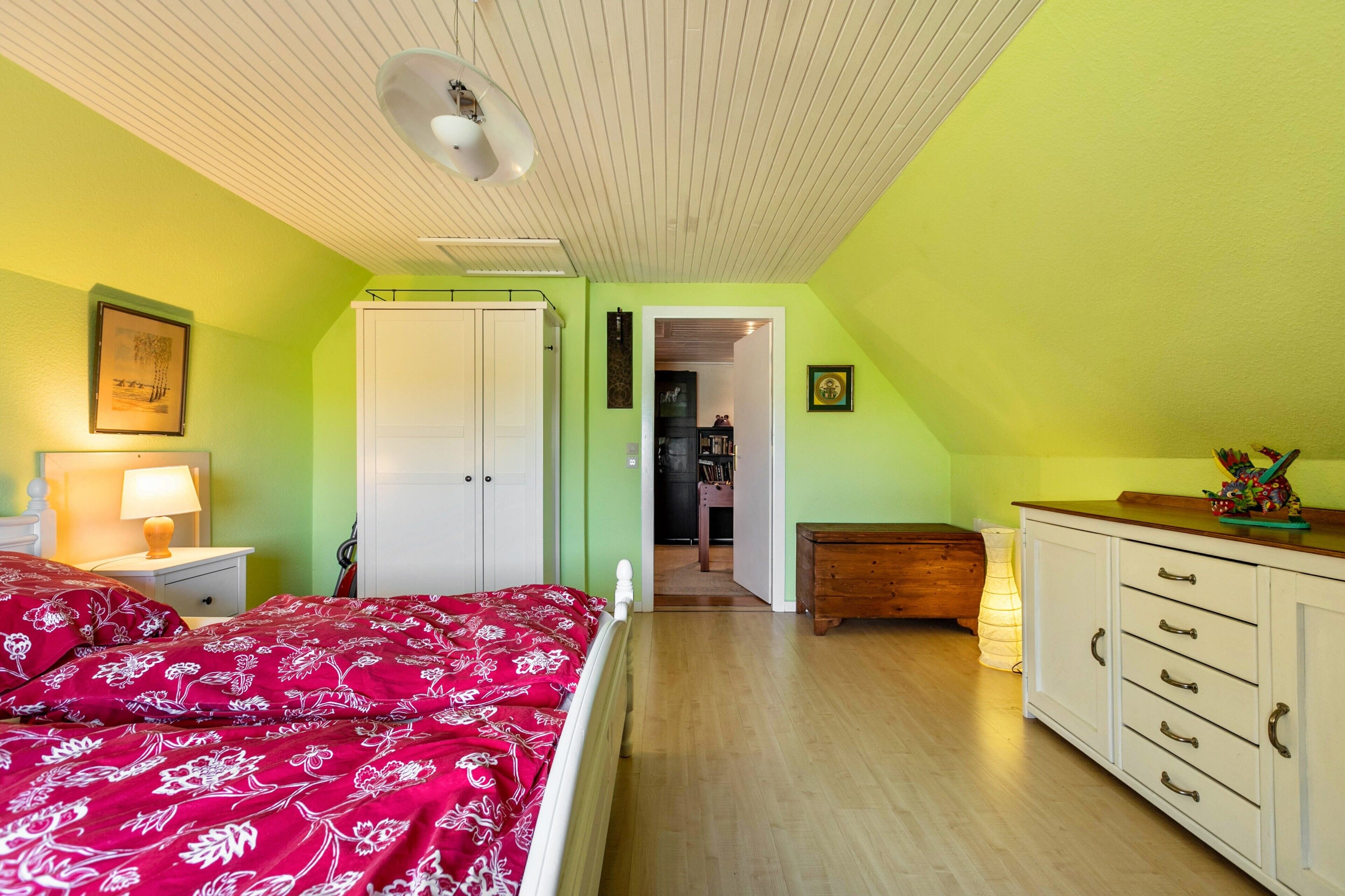 A bedroom with a bed, a nightstand, a dresser, and a door leading to another room.